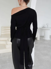 Person wearing a black off-shoulder top and black pants in a minimalistic setting.