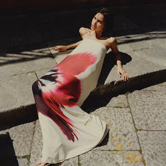 Woman lying on a stone pavement wearing a dress with a red and black abstract design.