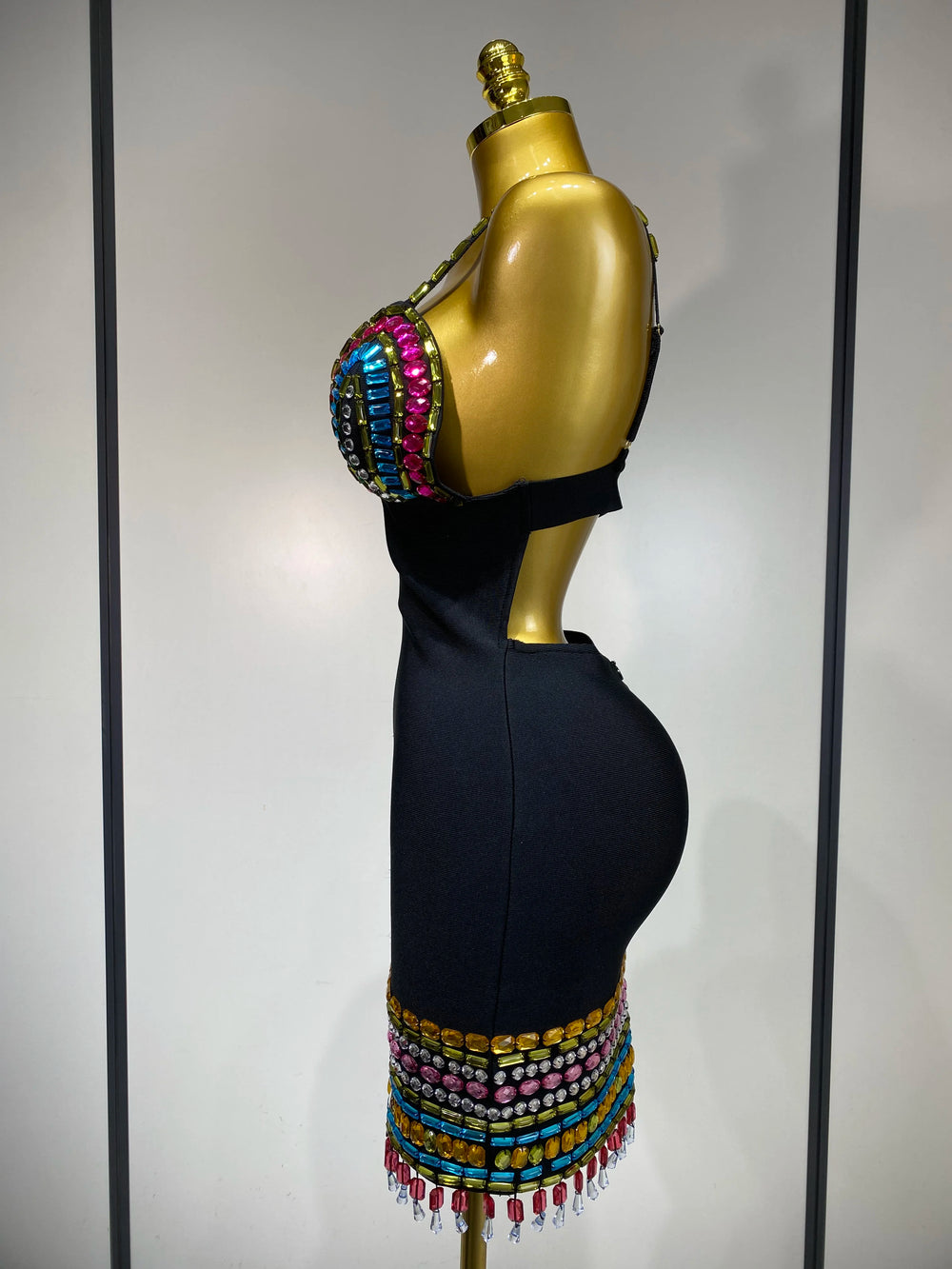 Mannequin wearing a black dress with colorful beaded details on a plain backgro