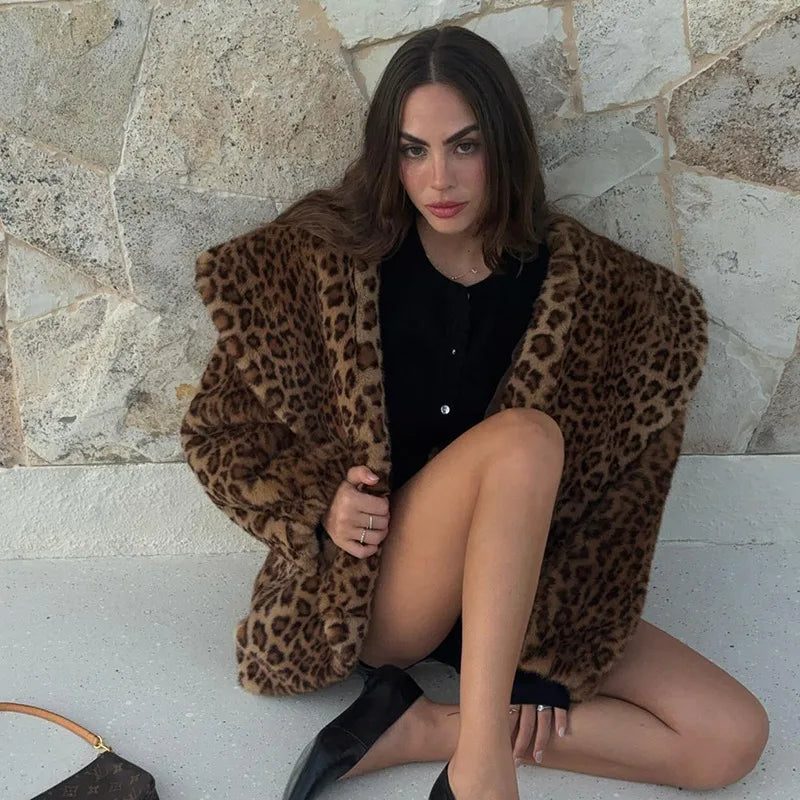 Woman wearing a leopard print coat sitting against a stone wall.