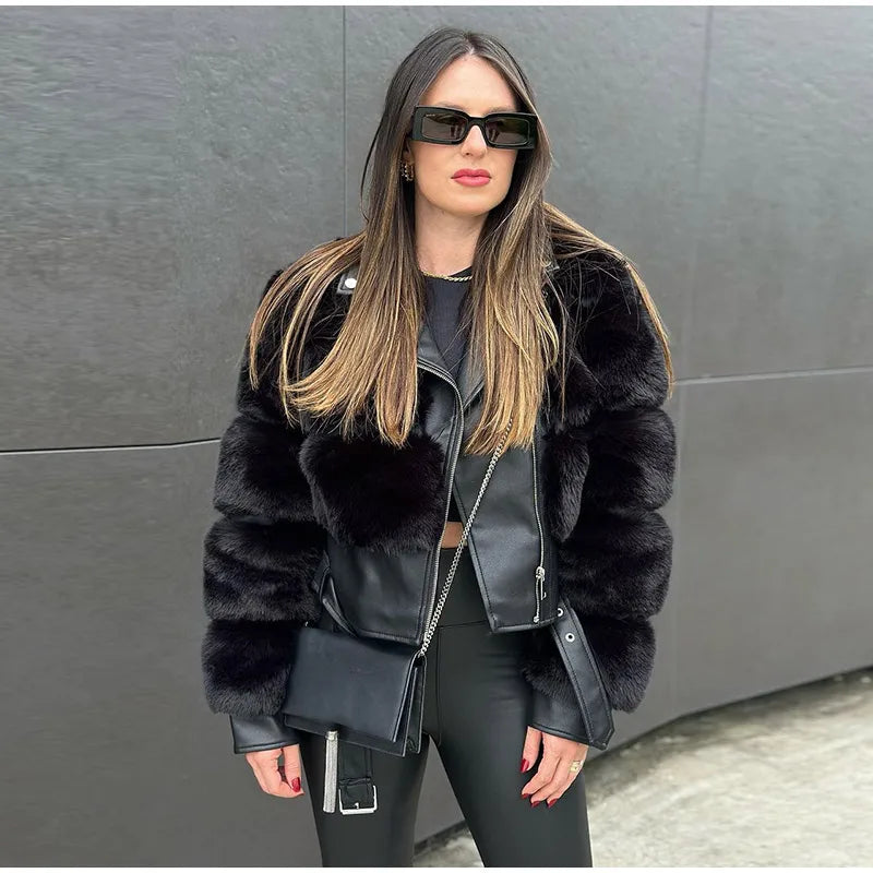 Woman wearing a black fur jacket and sunglasses against a gray wall.