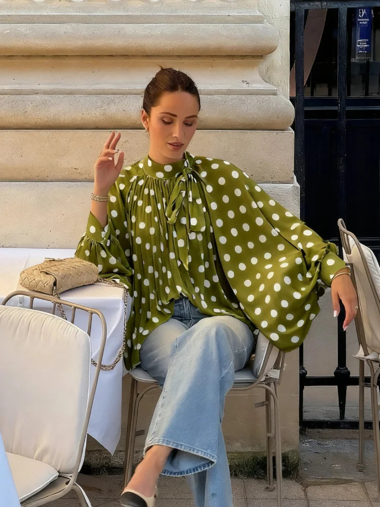 Woman in a green polka dot blouse and blue jeans sitting outdoors.