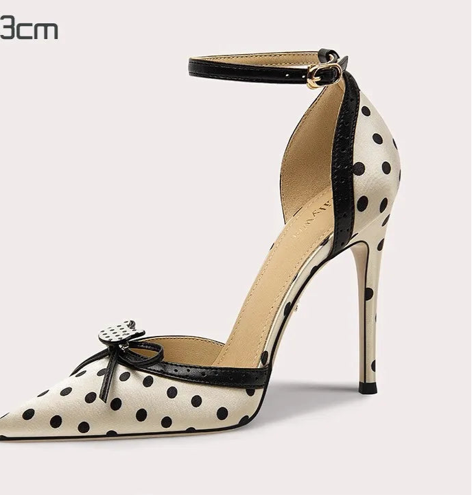 Polka dot high-heeled shoe with an ankle strap on a light gray background