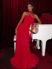 Woman in a red one-shoulder dress standing next to a white piano with red flowers.
