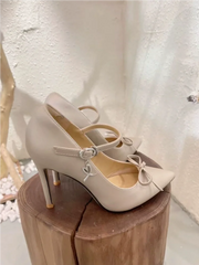 White high-heeled shoes with bow details on a wooden block against a light background