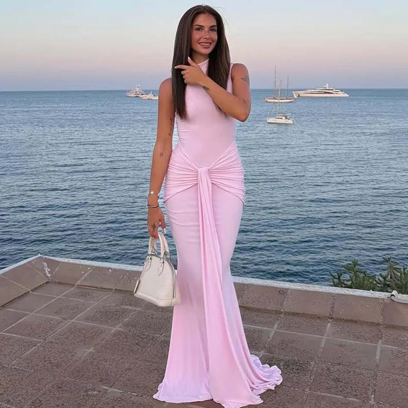 Woman in a pink dress standing by the sea with boats in the background