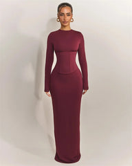 Woman wearing a burgundy long-sleeve gown against a plain background