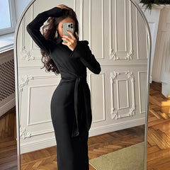 Person taking a mirror selfie wearing a black dress in a room with wooden flooring and white walls.