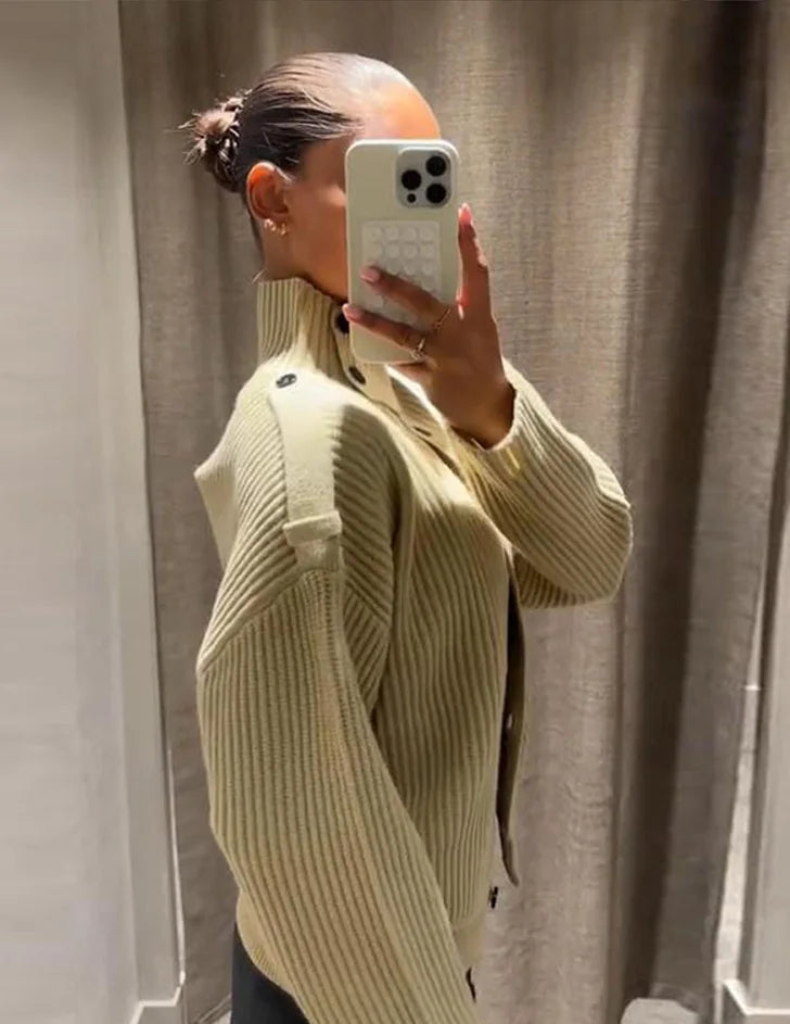 Person wearing a beige ribbed sweater taking a mirror selfie.