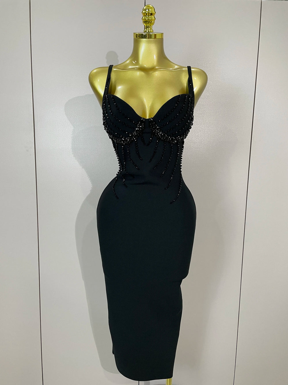 Black dress with bead detailing on a mannequin against a white background