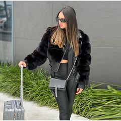 Woman in a black fur jacket and sunglasses pulling a suitcase outdoors.