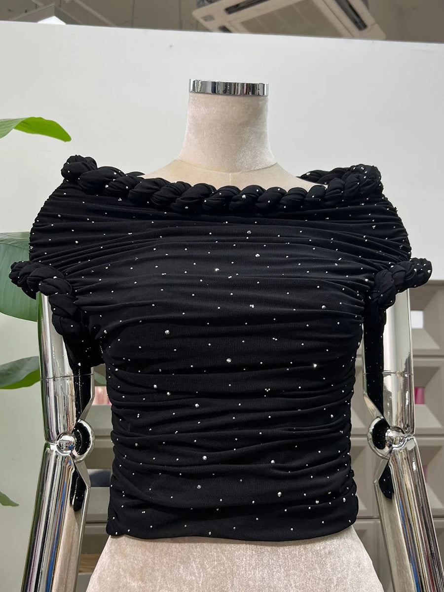 Black ruched top with embellishments on a mannequin against a white background