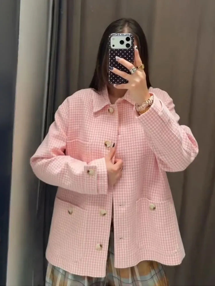 Person wearing a pink checkered jacket taking a mirror selfie.