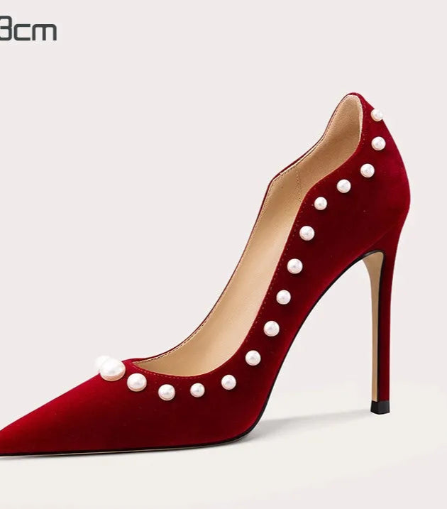 Red high-heeled shoe with pearl embellishments on a light gray background