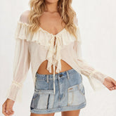 Woman wearing a sheer white blouse with ruffles and a denim skirt on a white background