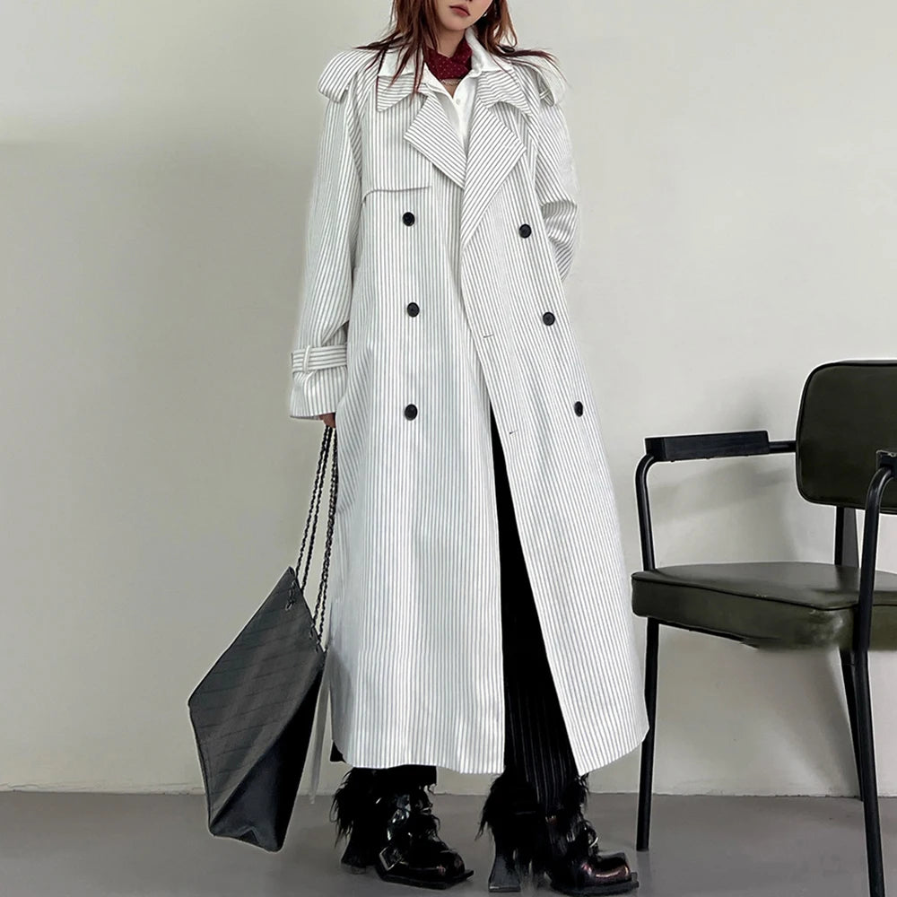 Person wearing a long black and white striped coat holding a black bag against a plain background.