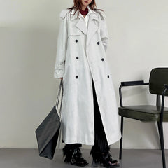 Person wearing a long black and white striped coat holding a black bag against a plain background.