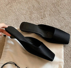 Black high-heeled shoes on a beige carpet with a white bag underneath.