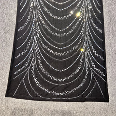 Black fabric with a spider web pattern made of small beads on a textured surface.