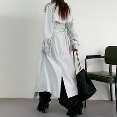 Person wearing a long, light-colored coat with a black chair in the background