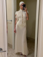 Person wearing a long beige dress with a high neckline and feather details, standing in a bathroom.