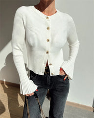 Person wearing a white ribbed cardigan with gold buttons against a neutral background