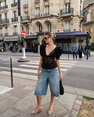 Woman walking on a city street wearing a black top and blue denim shorts.