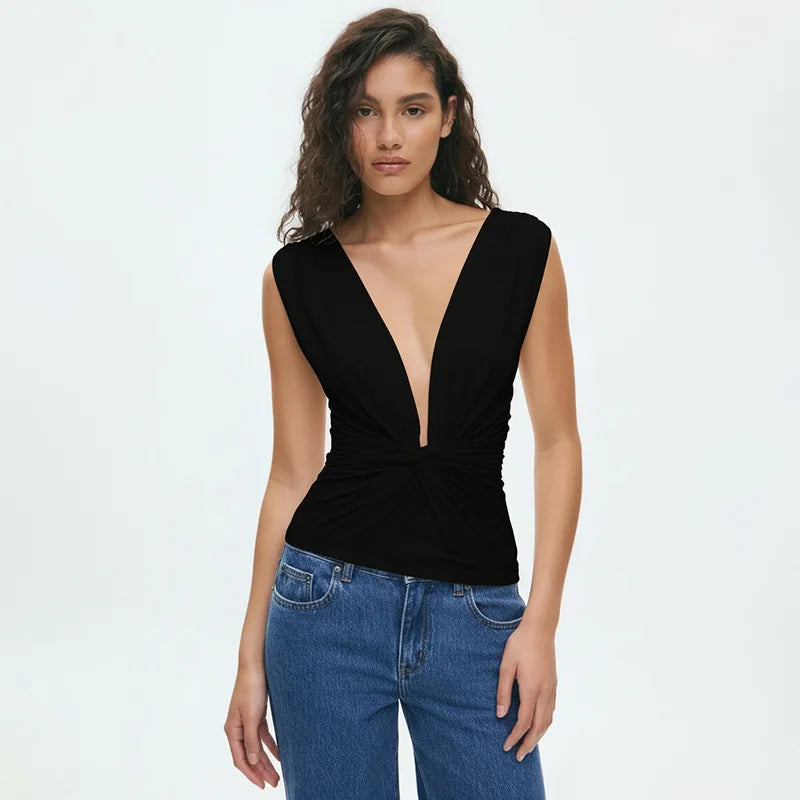 Woman wearing a black sleeveless top with a deep neckline and blue jeans on a white background