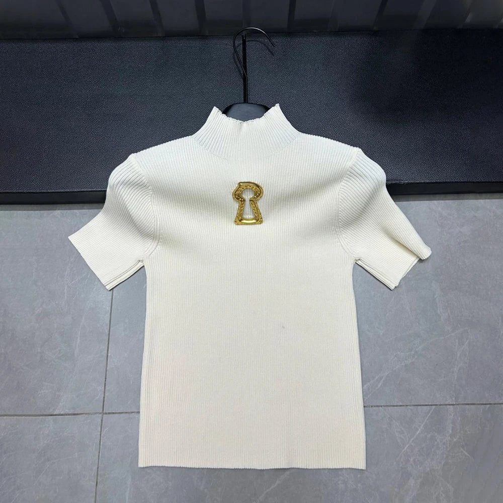 White turtleneck sweater with a gold emblem on a hanger against a dark background