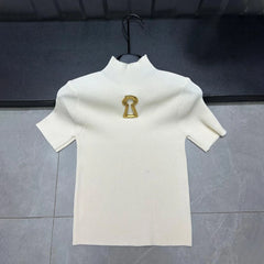 White turtleneck sweater with a gold emblem on a hanger against a dark background