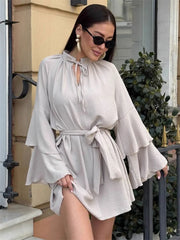 Woman wearing a light gray dress with bell sleeves standing outdoors.