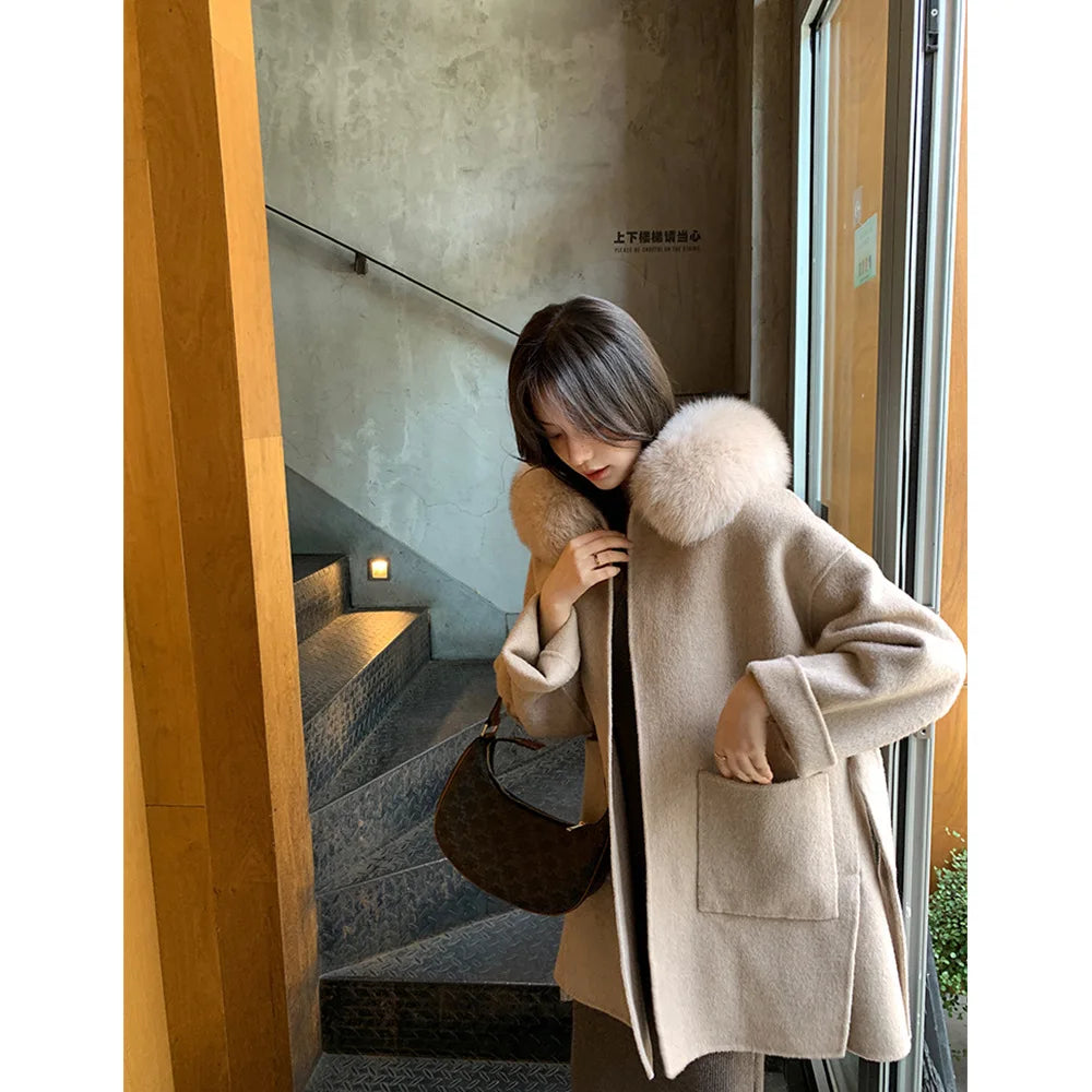 Woman wearing a beige coat with a fur collar in an indoor setting.