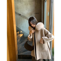 Woman wearing a beige coat with a fur collar in an indoor setting.