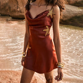 Woman in a red dress with gold starfish patterns standing by a body of water.