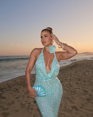 Woman in a light blue dress standing on a beach at sunset