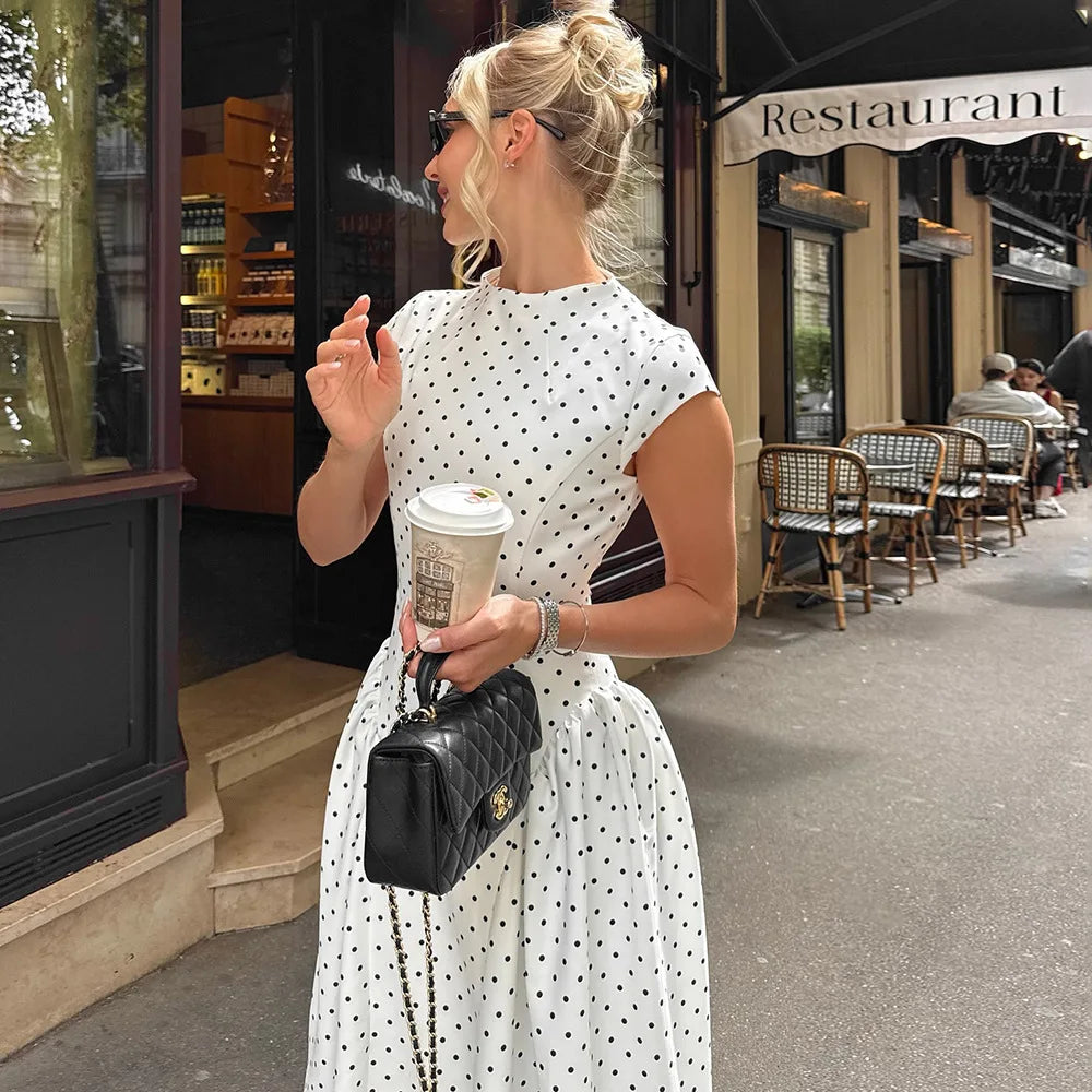 Woman in a polka dot dress holding a coffee cup on a city street.