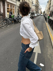 Person walking on a city street wearing a white blouse and blue jeans.