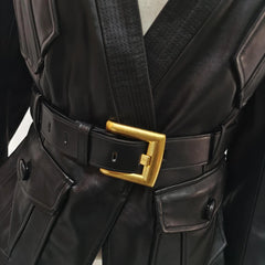 Close-up of a black leather outfit with a gold belt buckle on a neutral background