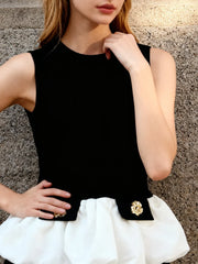 Person wearing a black sleeveless top with a gold brooch against a textured wall.