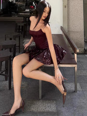 Woman in a burgundy dress with sequin skirt sitting on a bench outdoors.