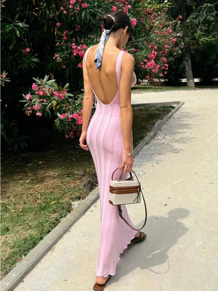 Woman in a pink dress with an open back walking on a sidewalk with pink flowers in the background