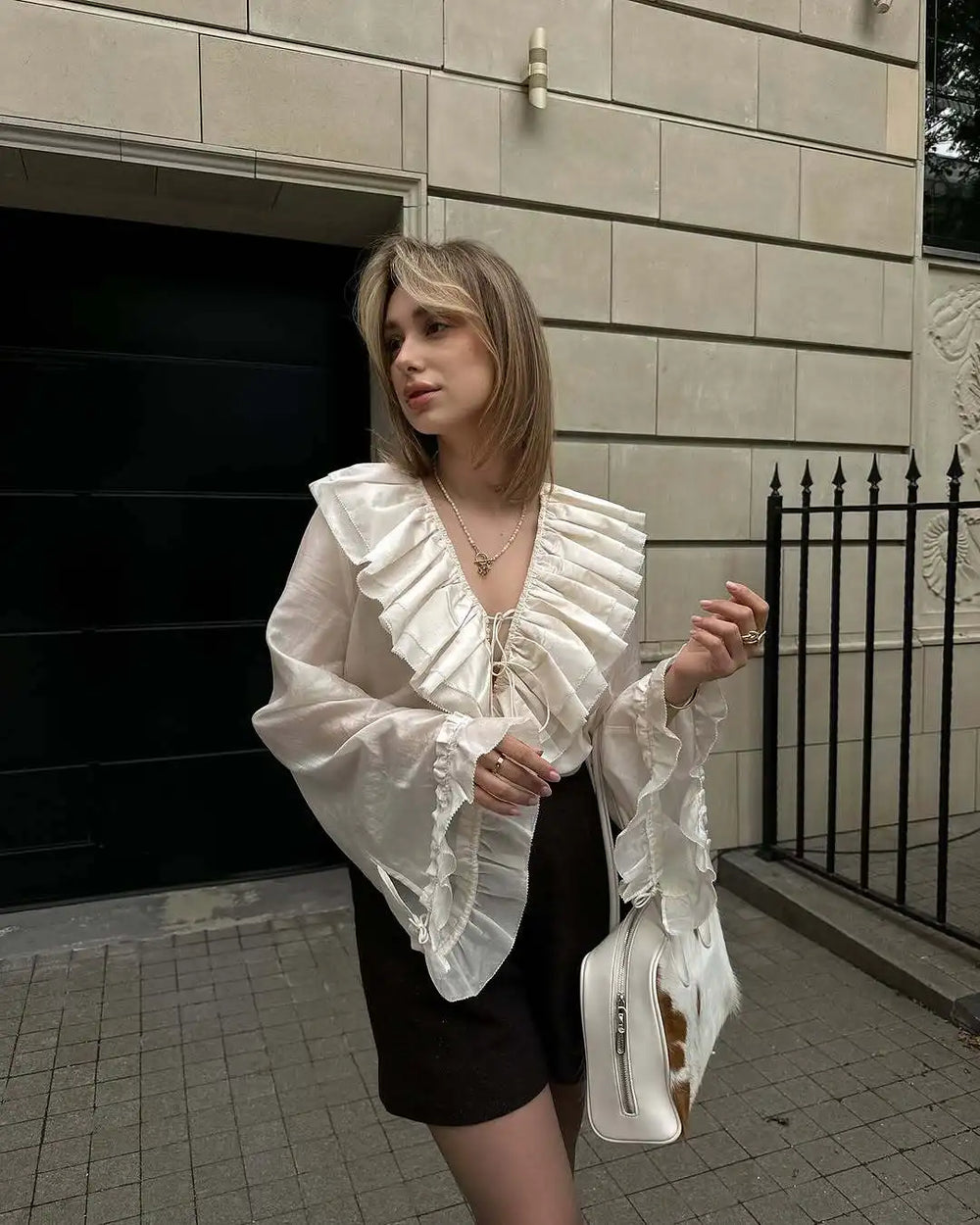 Woman wearing a white ruffled blouse and black skirt standing in front of a building.