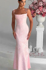 Woman in a pink lace dress standing next to a floral arrangement indoors.