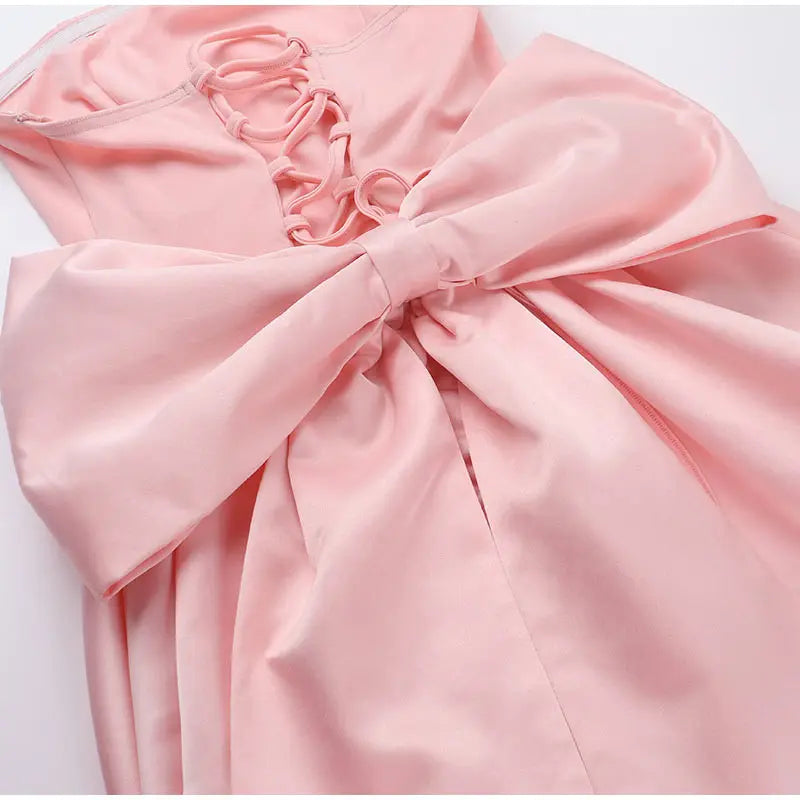 Close-up of a pink satin dress with a large bow on a white background