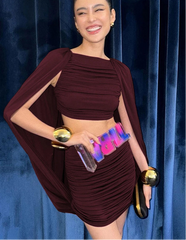 Woman in a burgundy outfit holding an award against a blue curtain background