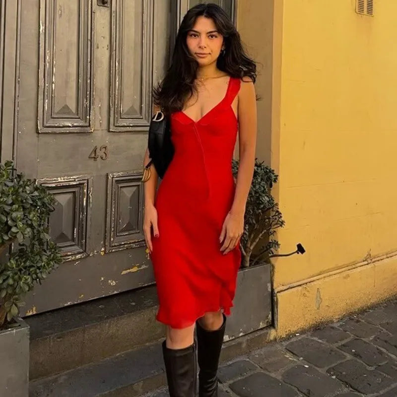 Woman in a red dress standing on a street with a yellow wall and gray door in the background.