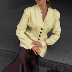 Woman wearing a light yellow blazer with black buttons on a dark background