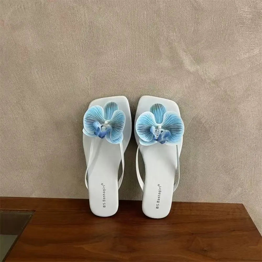 White sandals with blue flower decorations on a wooden surface and beige wall background