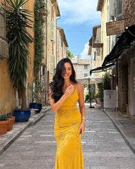 Woman in a yellow dress standing on a picturesque street with buildings and plants.
