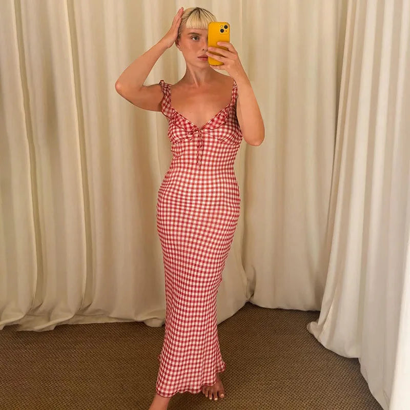 Woman taking a mirror selfie wearing a red and white checkered dress against a beige curtain background.